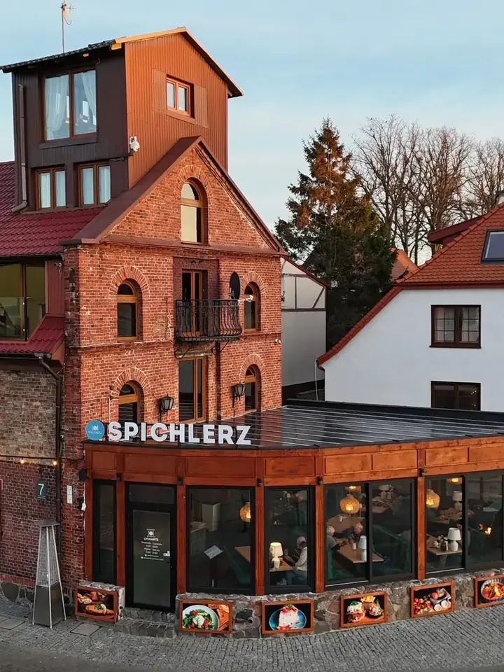 Ceglana fasada zabytkowego spichlerza z szyldem Spichlerz i przeszklonym pawilonem restauracji